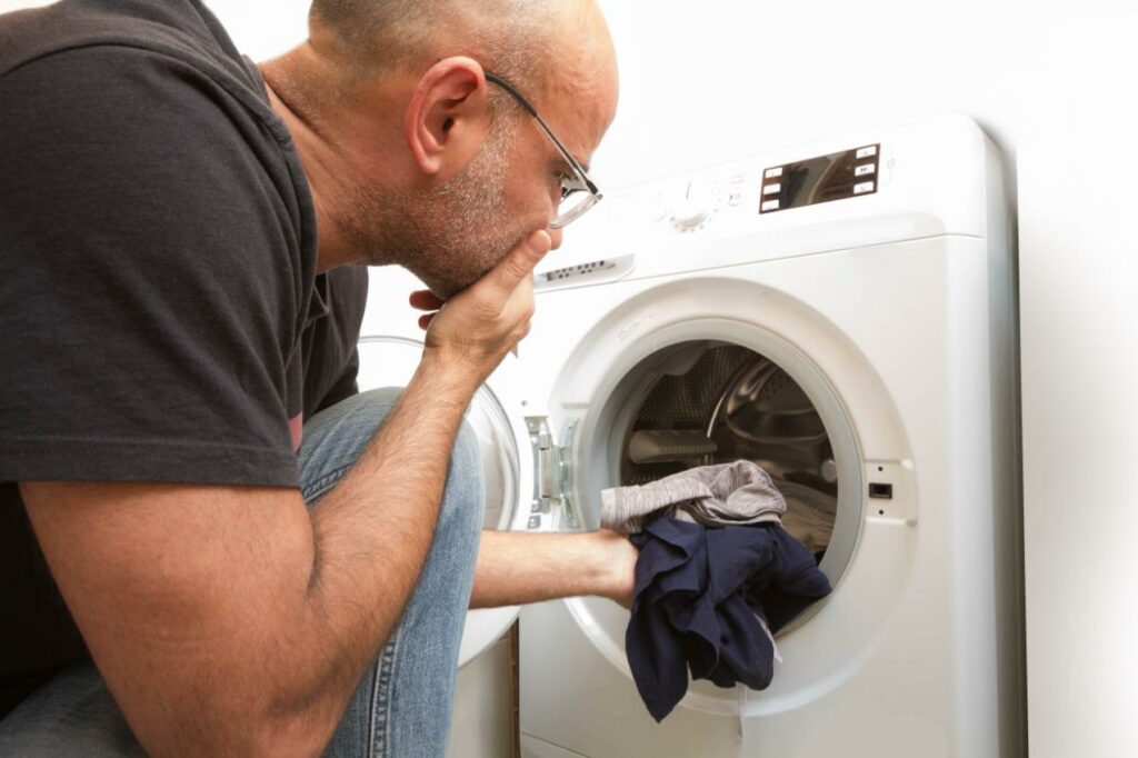 bald-man-gray-jeans-t-shirt-sits-front-washing-machine-home-load-washing-machine-with-dirty-clothes-bright-spacious-living-room-with-modern-interior